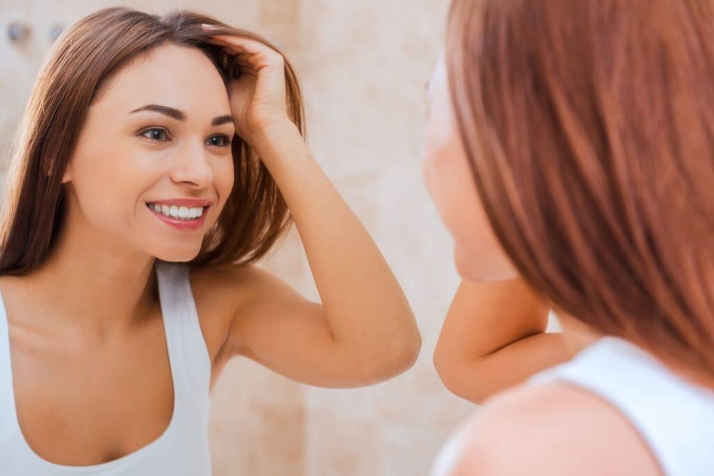 Woman smiling in mirror with smooth skin and healthy hair after using Ariessence PDGF+ for non-invasive rejuvenation