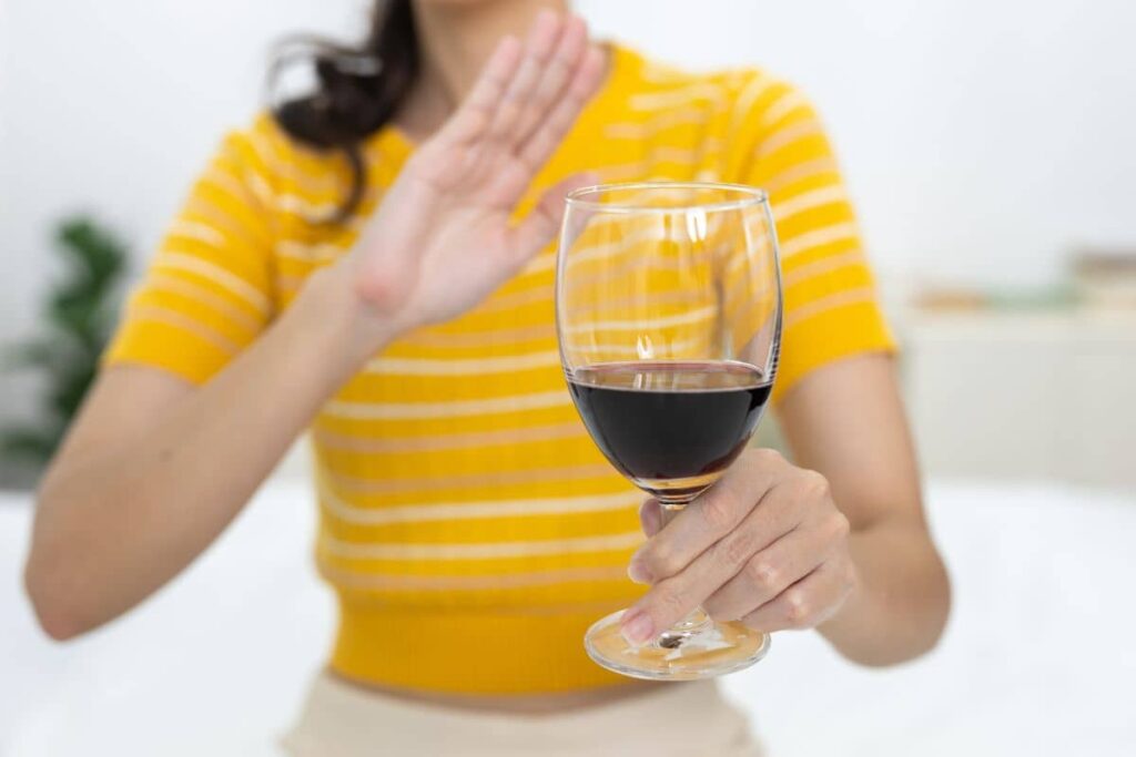 Woman refusing a glass of red wine, following pre-surgery guidelines to avoid alcohol before facelift procedure.