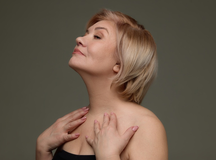 Mature woman touching neck and chest illustrating candidacy for Radiesse décolleté treatment for wrinkles and crepey skin